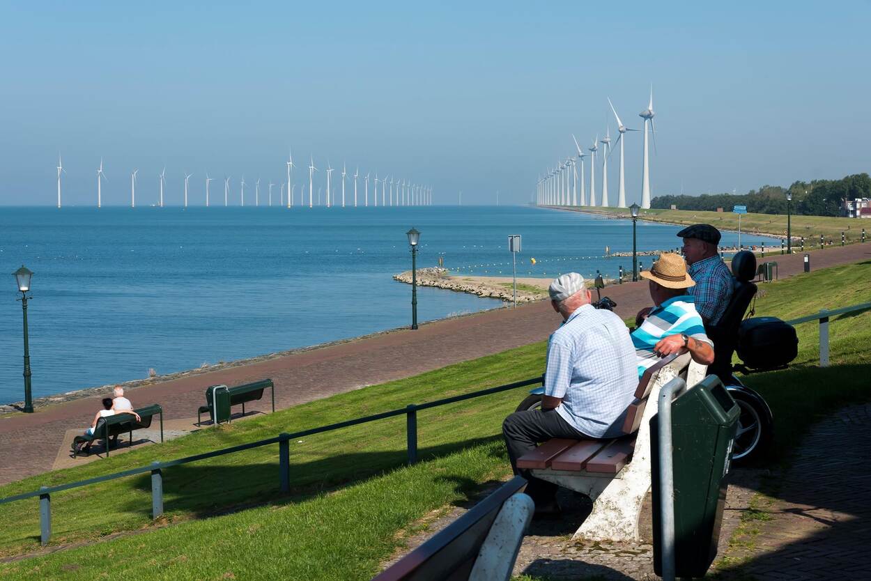 Mannen op bankje wijzen naar windmolenpark (bij Urk)